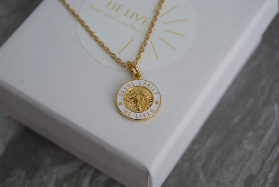 Gold He Lives necklace on its gift box
